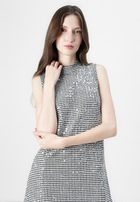 Hame dress tanpa lengan dengan pola gingham hitam dan putih, menampilkan kerah tinggi dan aksen berkilau yang halus di bagian depan.