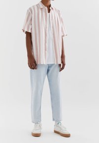 Kortebleeve gestreepte shirt in lichtroze en wit, gecombineerd met lichtblauwe jeans en witte sneakers met beige zolen.