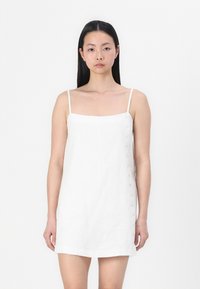 White linen dress with thin straps, square neckline, and button accents along the left side. Smooth texture and knee-length design.