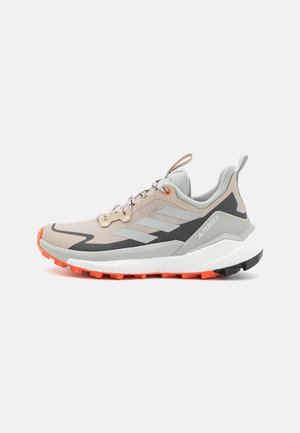 Chaussure de trail Adidas Terrex beige et grise avec des détails noirs et orange sur la semelle, des lacets et un col de cheville rembourré.