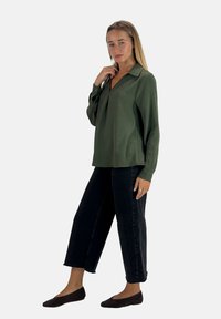 Groene blouse zonder kraag met een ontspannen pasvorm, lange mouwen en een gestructureerde afwerking, gecombineerd met hooggetailleerde zwarte wijde spijkerbroek en bruine ballerina's.