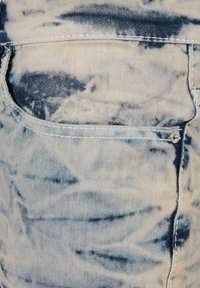 Denim tkanina svijetloplave boje s tie-dye uzorcima. Ima stražnji džep s kontrastnim šavovima i metalnim gumbom.