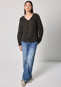 Halenka s leopardím vzorem v černé a hnědé barvě, dlouhé rukávy, výstřih do V a nařasené detaily, doplněná o světle modré kalhoty s širokými nohavicemi a tenisky.