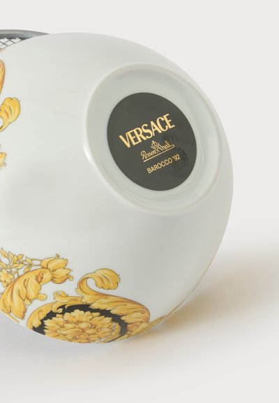Λευκό πορσελάνινο μπολ Versace με χρυσά λουλουδάτα μοτίβα Barocco και μαύρη κυκλική ετικέτα με την επιγραφή "Versace Rosenthal Barocco '92" στη βάση του.