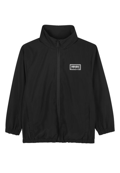 Veste noire avec col montant, fermeture éclair, poignets et ourlet élastiques. Présente un logo de marque blanc rectangulaire sur la poitrine gauche. Texture lisse.