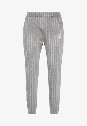 Pantalones de chándal grises con finas rayas verticales blancas, cintura y puños elásticos, con un pequeño logotipo bordado en blanco en el muslo izquierdo.