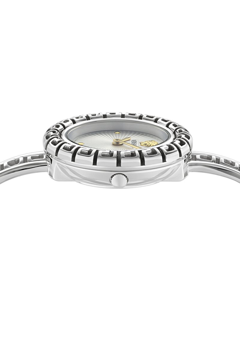 Srebrny zegarek na rękę z wzorzystą lunetą, złotymi akcentami na tarczy i koroną z boku, pochylony, aby pokazać tarczę zegarka i pasek.