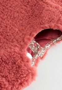 Puchaty sweter z koralików o teksturowanej tkaninie, z kwiatowym nadrukiem na podszewce i szerokim wycięciem na ramionach dla większej wygody.