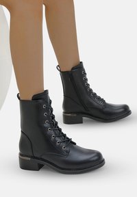 Bottines en cuir noir avec un devant à lacets, fermeture éclair sur le côté, bout arrondi et petit talon carré. Dotées d'œillets en argent et d'une finition lisse.