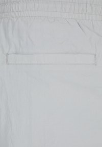 Ljust grå shorts tillverkade av ett lätt material med resårmidja och en enda rektangulär bakficka. Strukturerad yta med subtila linjer.