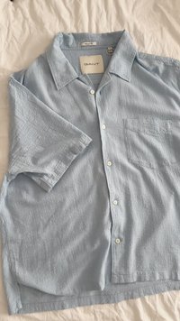 Kurze Ärmel, hellblaues Hemd aus strukturiertem Stoff, mit Knopfleiste und einer linken Brusttasche. Mit einem lässigen Kragen und dezentem Muster.