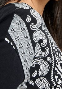 Czarna odzież z materiałem w biały wzór paisley i geometryczne kształty. Gładka tekstura, dopasowany krój i krótkie rękawy.