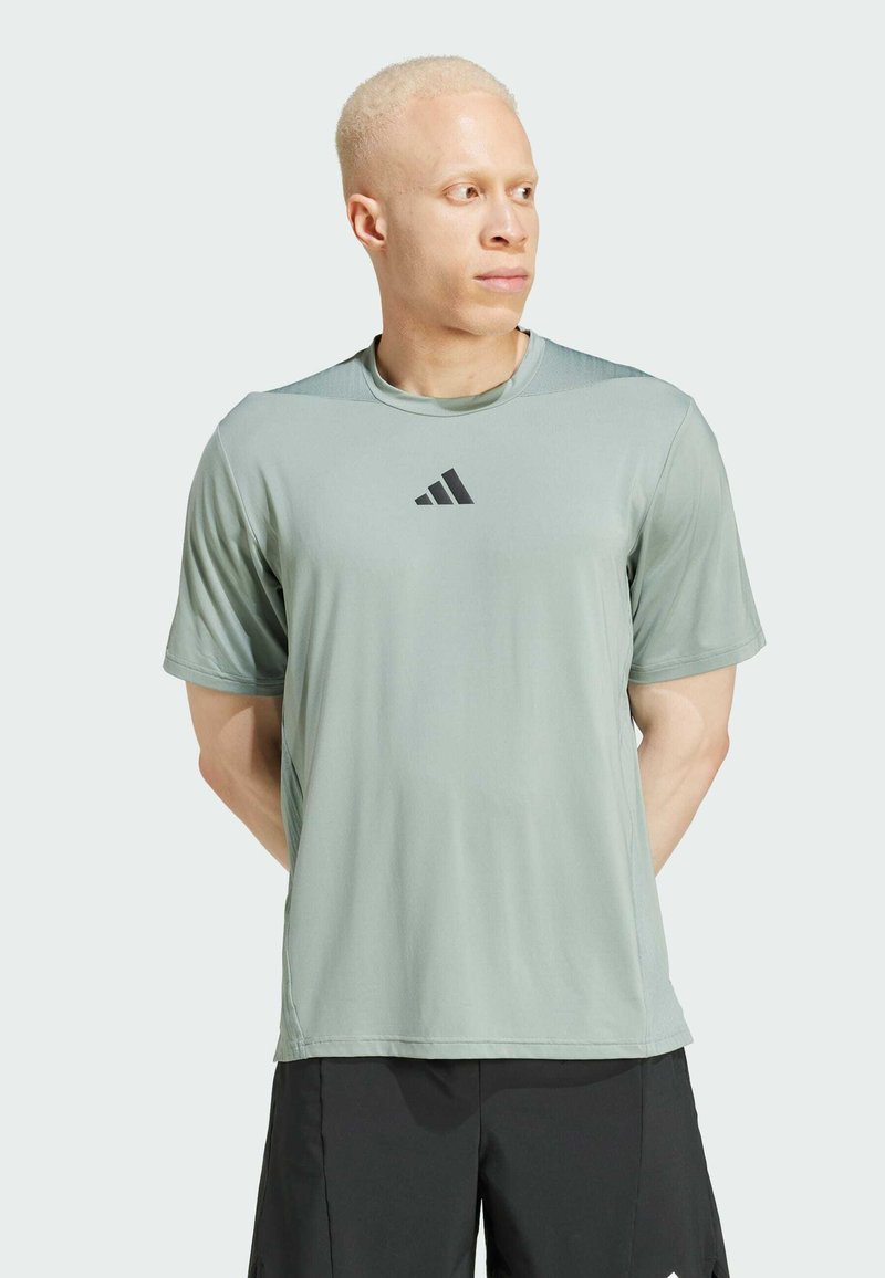 Lys grøn kortærmet træningsshirt lavet af glat stof, med et sort Adidas-logo på brystet og en afslappet pasform.
