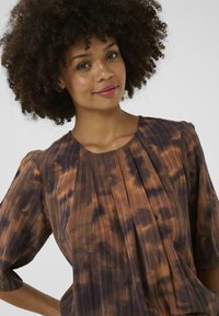 Blouse à motifs marron et violet avec des manches courtes, design plissé et encolure arrondie, fabriquée en tissu léger et texturé.