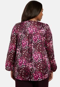Blusa a maniche lunghe con uno sfondo di borgogna intenso, caratterizzata da un vivace motivo astratto in rosa e bianco. Tessuto leggero con una vestibilità rilassata.