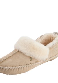 Beige suède pantoffel met een pluizige crèmekleurige bontkraag, gedetailleerde stiksels en een klein metalen merkembleem. Zachte textuur overal.