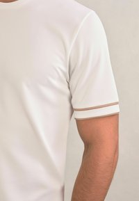 Biela krátka t-shirt s textúrovaným vzorom. Má hnedé akcentové pruhy na rukávoch. Ľahký materiál, okrúhly výstrih.