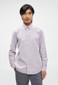 Ljust lila randig långärmad skjorta med knappad krage, med rak nederkant och vita knappar. Slät tygtextur.