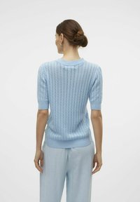 Maglione azzurro chiaro a maglia con maniche corte, scollo rotondo e una trama aperta; abbinato a pantaloni azzurri chiari.