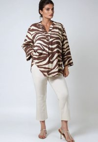 Brown and cream striped blouse with a v-neckline, loose fit, and three-quarter sleeves, paired with cream pants and strappy heels.