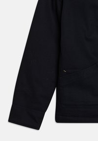 Dunkelblaues Langarmhemd aus strukturiertem Stoff mit sichtbaren Nähten und einer Brusttasche mit gelben Akzenten.