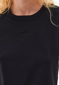 Sort sweatshirts med ribbet rund hals og en subtil V-formet sømdetalje. Stoffet ser blødt ud med en glat tekstur.