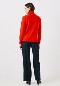 Maglione rosso a collo alto con una texture morbida, fitting slim, e polsini a coste, abbinato a pantaloni blu con righe e stivali neri con tacco.