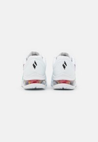 Weiße Sportschuhe mit einer mehrfarbigen Sohle, strukturiertem Lederoberteil und einem markanten Logo an der Ferse.