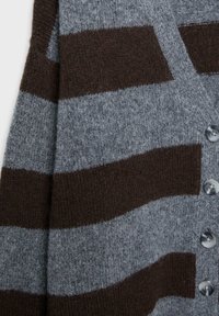 Sivý a hnedý pruhovaný kardigán z mäkkej vlny, s okrúhlymi gombíkmi a textúrovaným povrchom. Vertikálne pruhy sa striedajú v farbe.