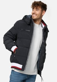 Puffer jacket in black with a hood, featuring a front zip, chest pocket, and ribbed cuffs with red and white stripes. Smooth texture.