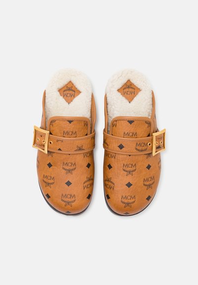Pantoufles en cuir brun à enfiler, dotées d'une doublure en polaire, d'un matériel en boucle dorée et d'un motif de logo MCM en relief sur toute la surface.