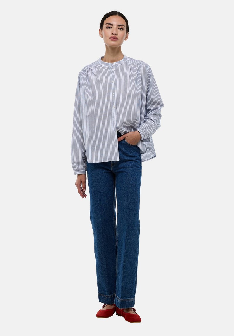 Chemise à rayures bleu clair et blanche, coupe décontractée. Assortie à un jean bleu taille haute et des ballerines rouges. Manches longues, col rond.