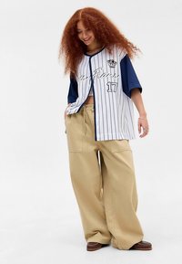 Balti un tumši zili svītrains īsroku džersijs ar numuru "17" un logo; kombinēts ar bēšām platajiem bikšu galiem un brūnām kurpēm.