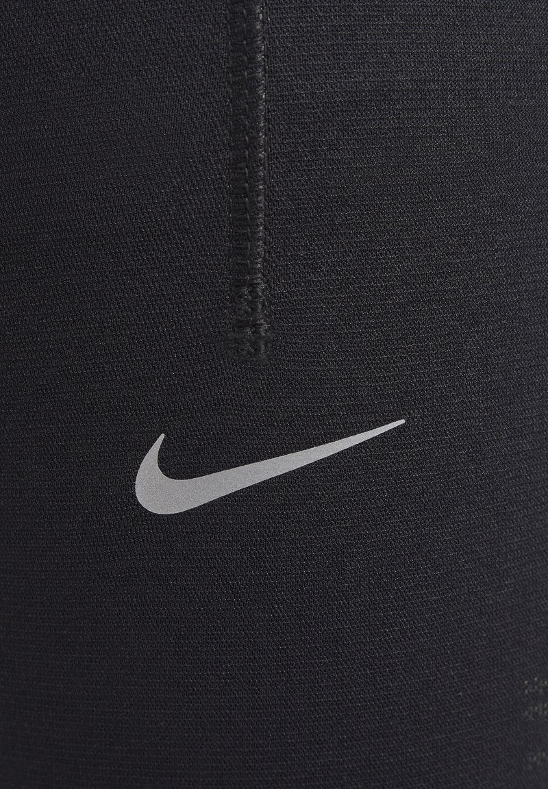 Leggings de sport noirs en tissu extensible, avec une couture visible et un petit logo Nike argenté sur le côté.