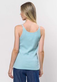 Šviesiai mėlynas ribuotas marškinėlių liemenėlis su plonomis petnešėlėmis, pasižymintis lygiu paviršiumi ir aptemptu siluetu, dėvimas su platesnėmis džinsinėmis kelnėmis.