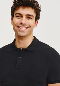 Czarna koszulka polo z teksturowanej tkaniny, z kołnierzykiem i zapięciem na dwa guziki, z haftowanym logo na piersi.