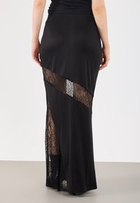 Μαύρη μάξι φούστα με εφαρμοστή μέση και στρώσεις από δαντελωτά κοψίματα, που δημιουργούν ασύμμετρο σχέδιο με λεία υφή υφάσματος.