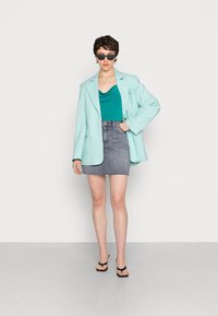 Blazer oversized em azul claro, top teal, saia mini de jeans cinza, chinelos pretos e óculos de sol pretos. Texturas suaves, estilo casual.