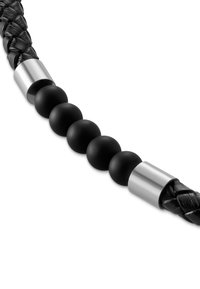 Sort fletet læderled med glatte matte sorte perler og sølv cylindriske detaljer. Fokus på tekstur og kontrasterende materialer.