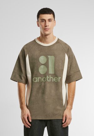 Olivengrøn oversized T-shirt med mat finish, prydet med et dristigt grafisk print i en lysere grøn farve og cremefarvede sidelapper. Blød tekstur.