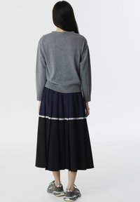 Pull en tricot gris, jupe plissée bleu marine et noir avec une bordure en dentelle, associés à des baskets grises. Texture lisse et design décontracté.