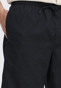 Mustad, kerged kangast püksid elastse vöökohaga, paelaga ja küljetaskutega. Sile tekstuur ja sirge säärega disain.