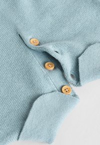 Pull en tricot bleu clair avec une finition texturée, présentant un col arrondi et trois boutons en bois le long de la patte de boutonnage.