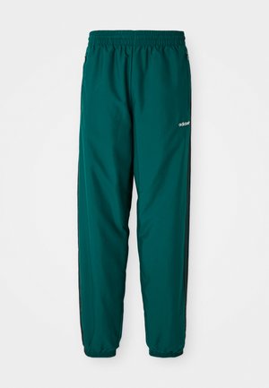 Calças desportivas verdes feitas de um tecido leve, com um cós elástico, bolsos laterais e riscas pretas nas laterais. Logótipo da Adidas visível.