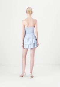 Šviesiai mėlyna bepečių suknelė su prigludusia liemene ir sluoksniuotais volanais rankovėse. Glotnus audinys su nedideliu blizgesiu. Dėvima su kreminėmis kulniuko bateliais.