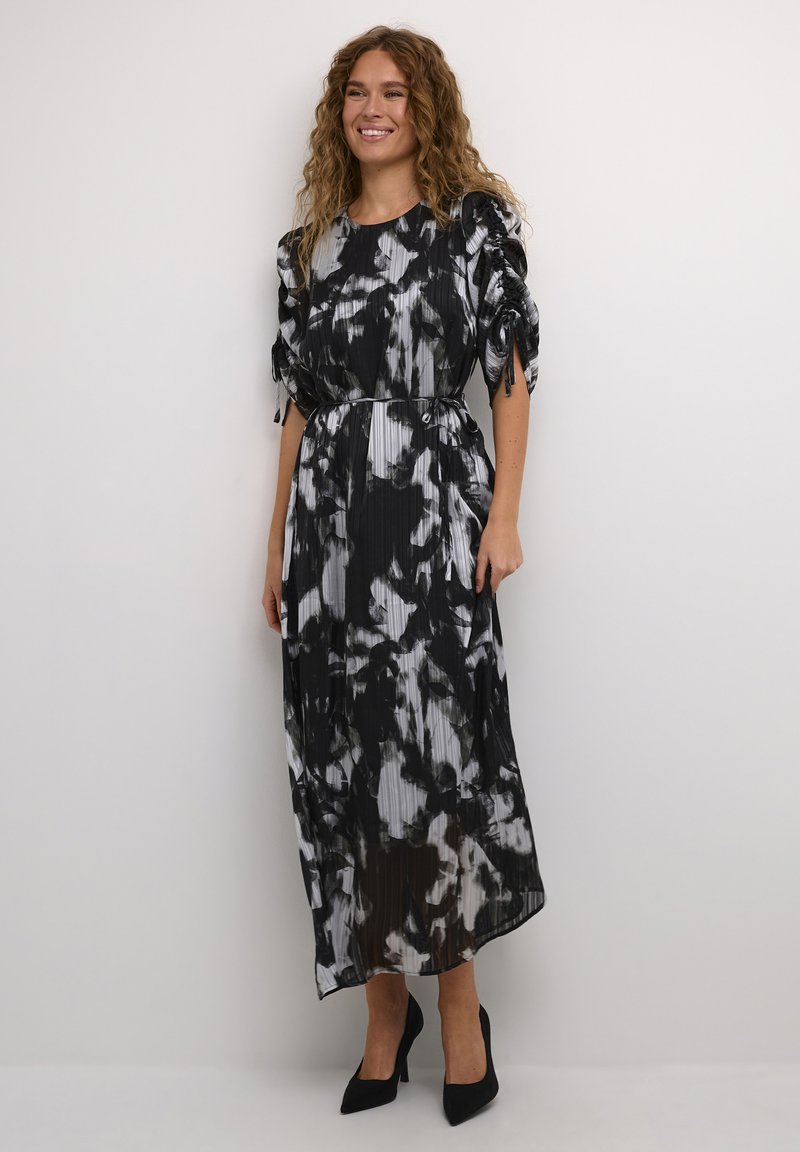 Zwart-witte tie-dye maxi jurk met korte pofmouwen,Gathered taille en verticale plooien. Gepaarde met zwarte hoge hakken.