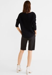 Pull noir surdimensionné, short rayé et bottines blanches jusqu'aux chevilles. Le pull a des manches longues et un col large. Le short arrive au niveau des genoux.