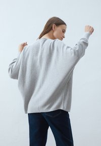 Světle šedý oversized svetr z měkké pleteniny s uvolněným střihem, spadlými rameny a texturovaným povrchem. Kombinujte s tmavými džíny.