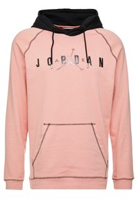 Felpa rosa con cappuccio nero, dotata di cordini neri e tasca a marsupio. Sul davanti è presente un logo "JORDAN" con un grafico Jumpman.