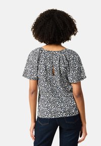 Blusa con stampa floreale, maniche corte a palloncino, sfondo scuro, fiori bianchi e blu, dettaglio sul retro a forma di chiave, tessuto leggero.